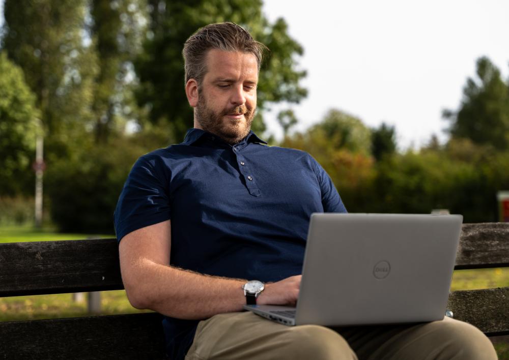 Man zit buiten op een bankje met laptop op schoot