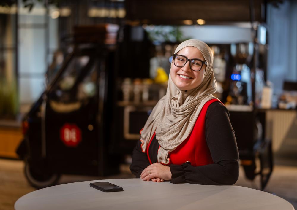 Mevrouw met hoofddoekje leunt tegen een statafel in moderne kantooromgeving