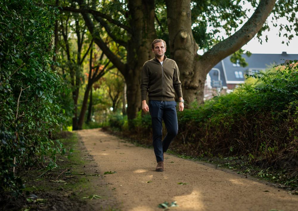 Man in bruine polo en nette broek loopt in park