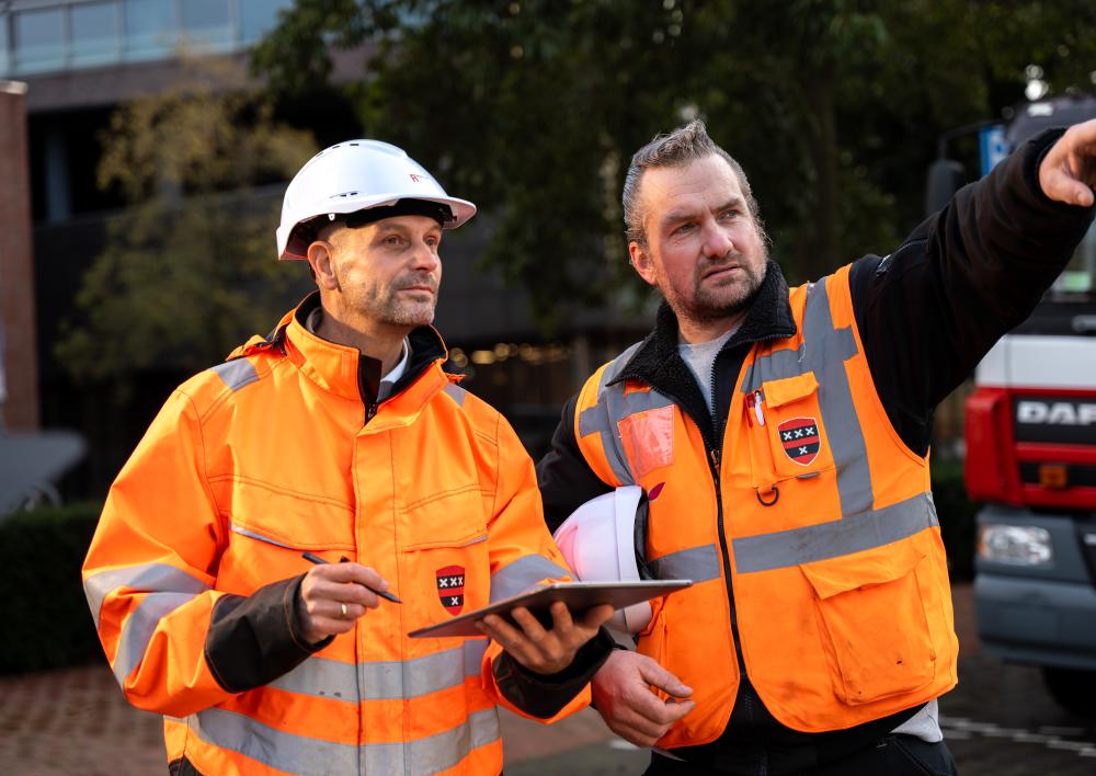 Twee werkvoorbereiders met oranje werkjassen aan wijzen naar project