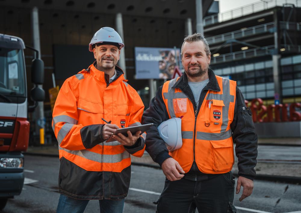 Twee medewerkers in oranje werkkleding kijken in de camera