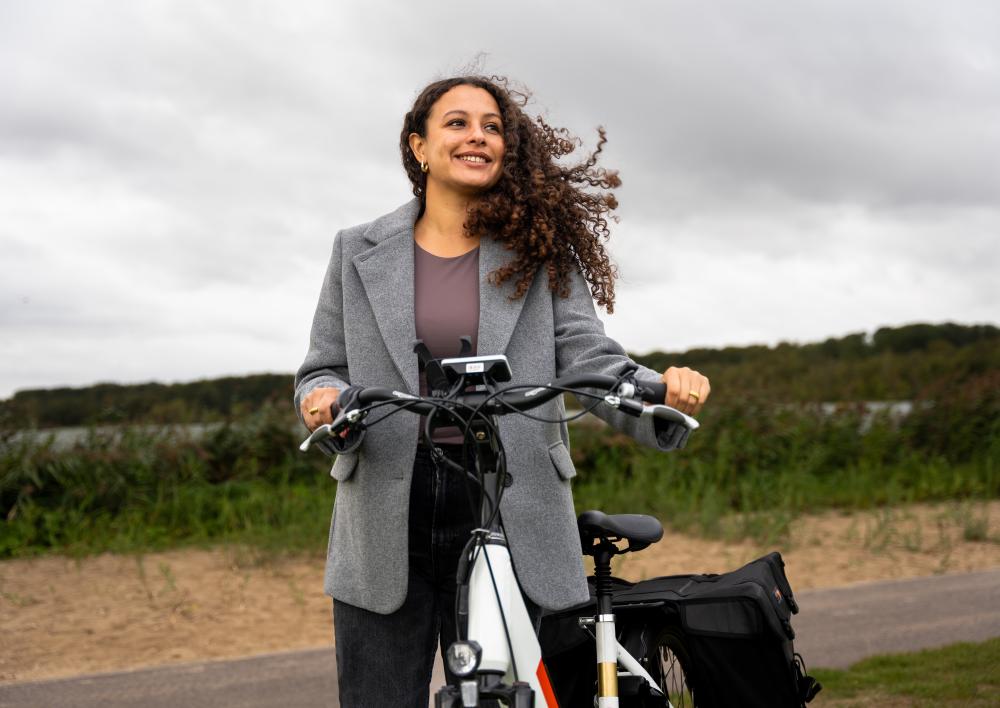 Vrouw kijkt lachend in de verte met fiets aan de hand