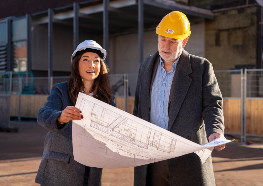 2 collega's met bouwhelm kijken op bouwplan bij project