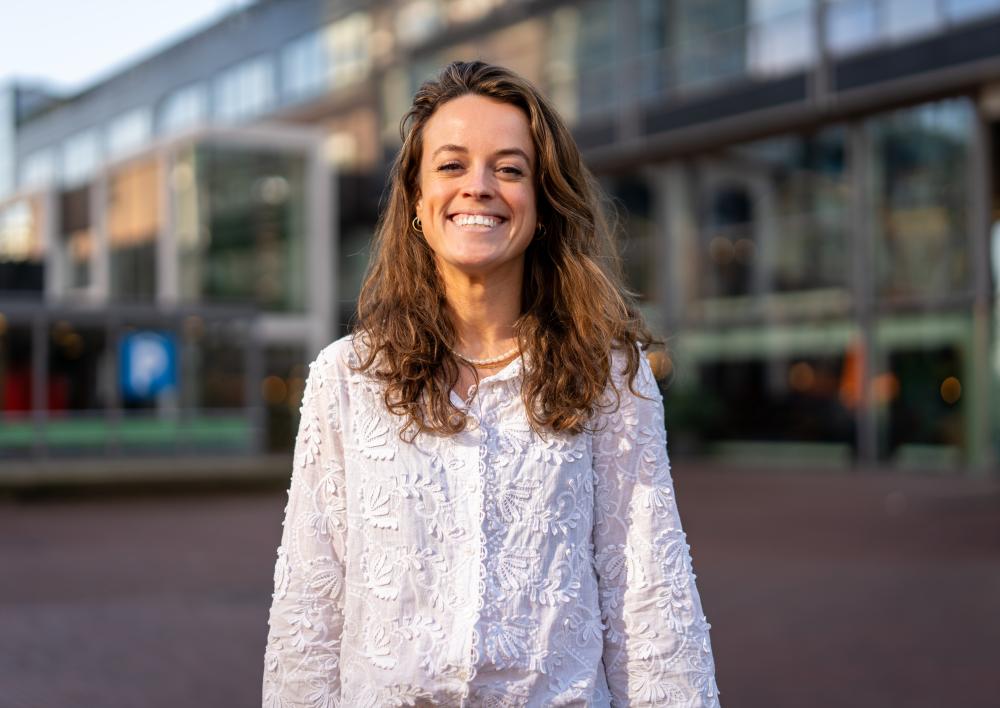 Medewerker kijkt lachend in camera buiten op een plein