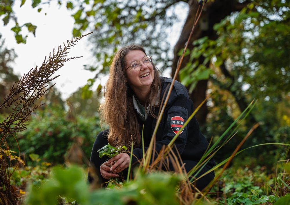 Medewerker zit hurkend tussen het groen in het openbare ruimte