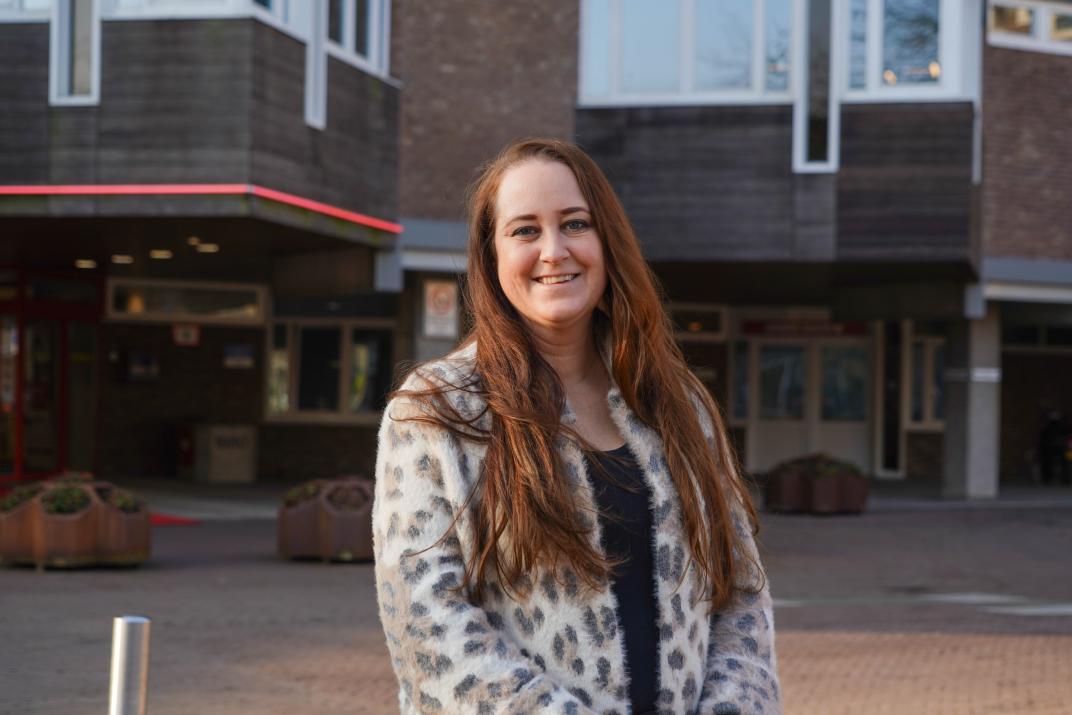 Stefanie staat voor het raadhuis en kijkt lachend in de camera