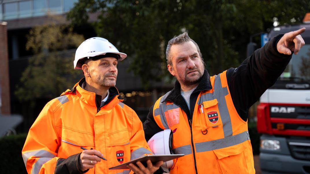 Twee collega's met oranje hesjes wijzen.