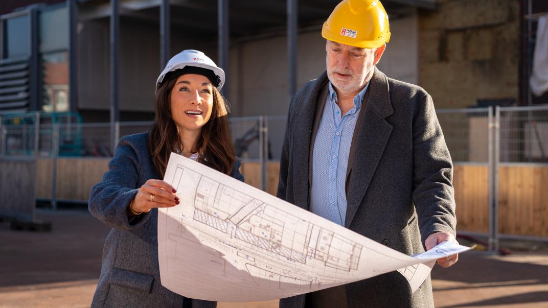 2 collega's met bouwhelm kijken op bouwplan bij project