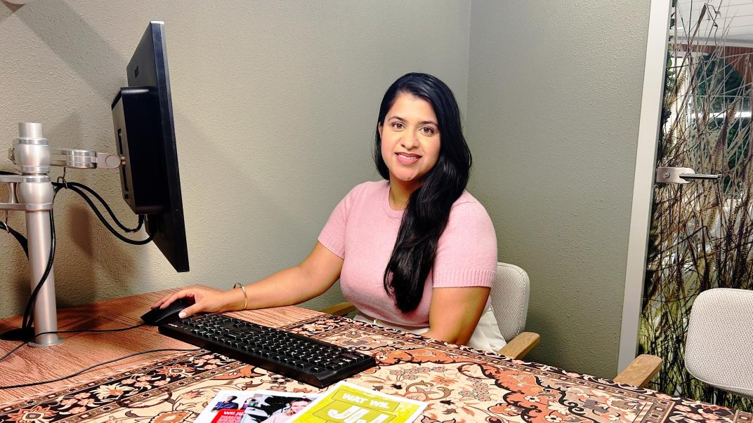 Madhavi in de bespreekruimte achter een beeldscherm met flyers voor haar
